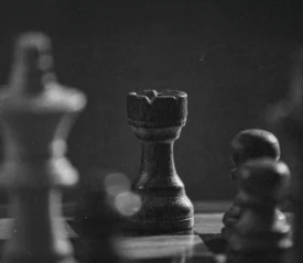 Black-and-white photograph of a chessboard with a wooden rook in sharp focus among blurred pieces