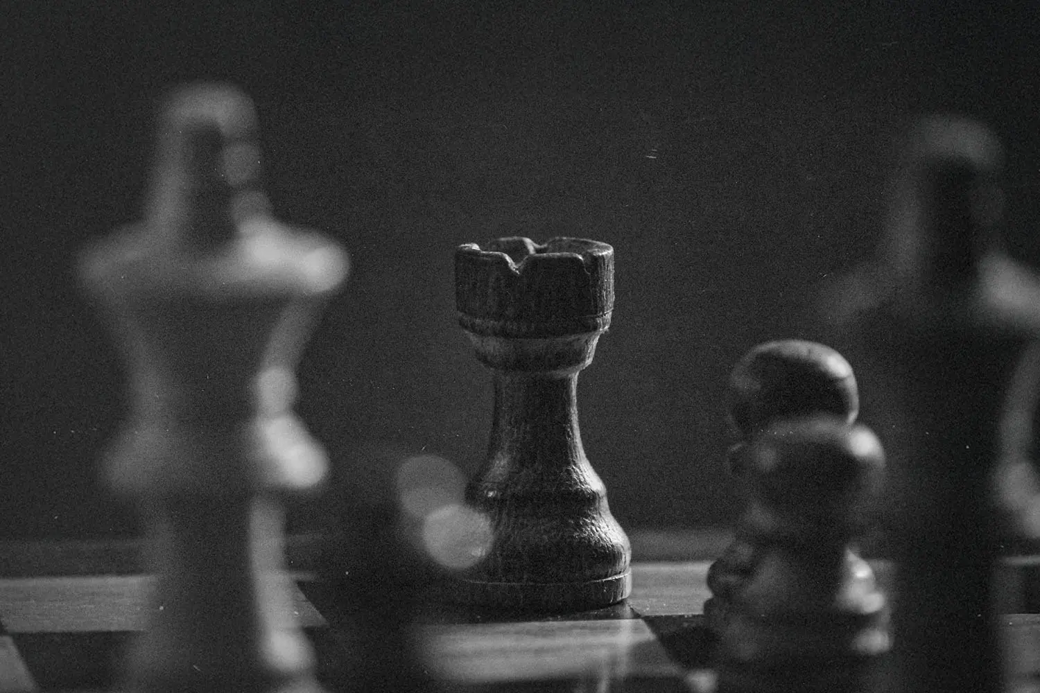 Black-and-white photograph of a chessboard with a wooden rook in sharp focus among blurred pieces