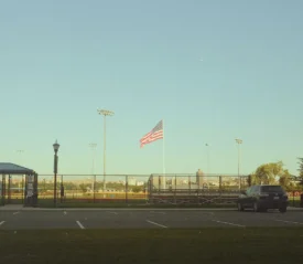 American flag flying in a ball field next to a parking lot