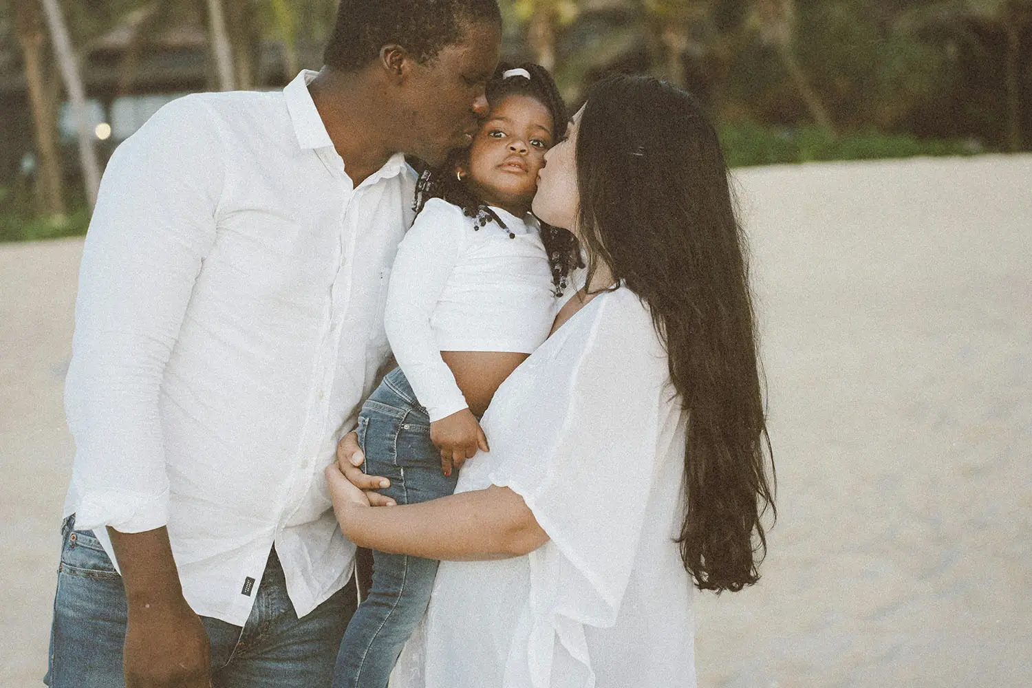 father and mother kissing their child