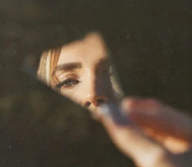 A hand holds a piece of cracked mirror with warm light illuminating the fingers