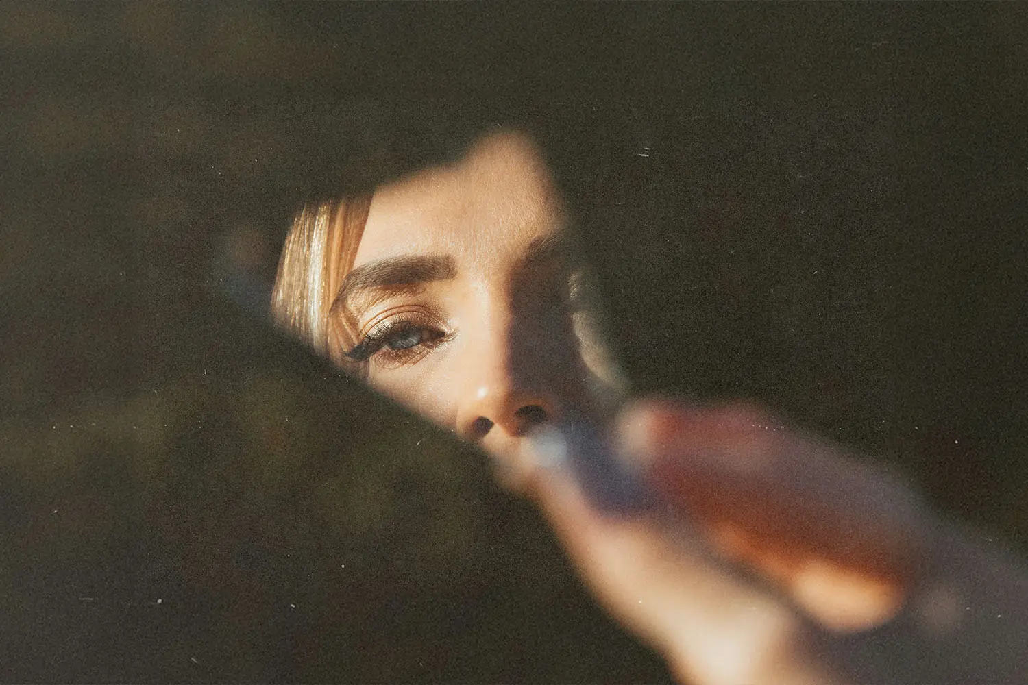 A hand holds a piece of cracked mirror with warm light illuminating the fingers