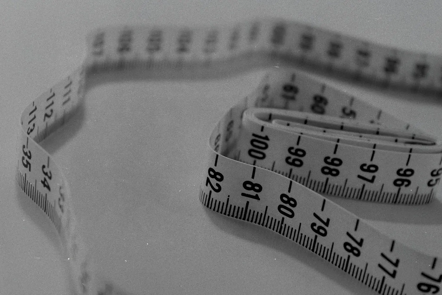 Flexible measuring tape coiled loosely on a flat surface in a black‑and‑white image