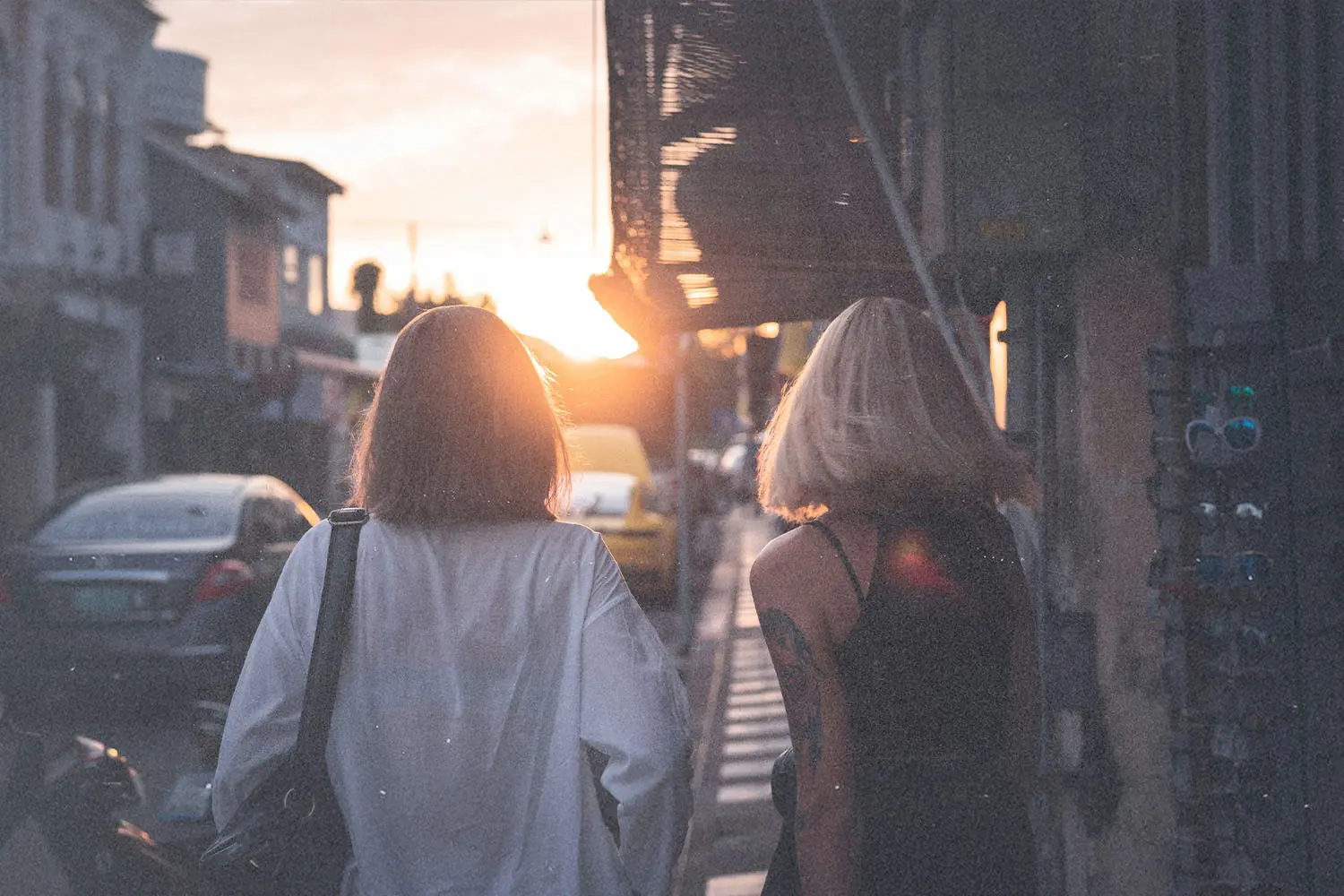 Two women walking down a city street at sunset with warm light shining between buildings