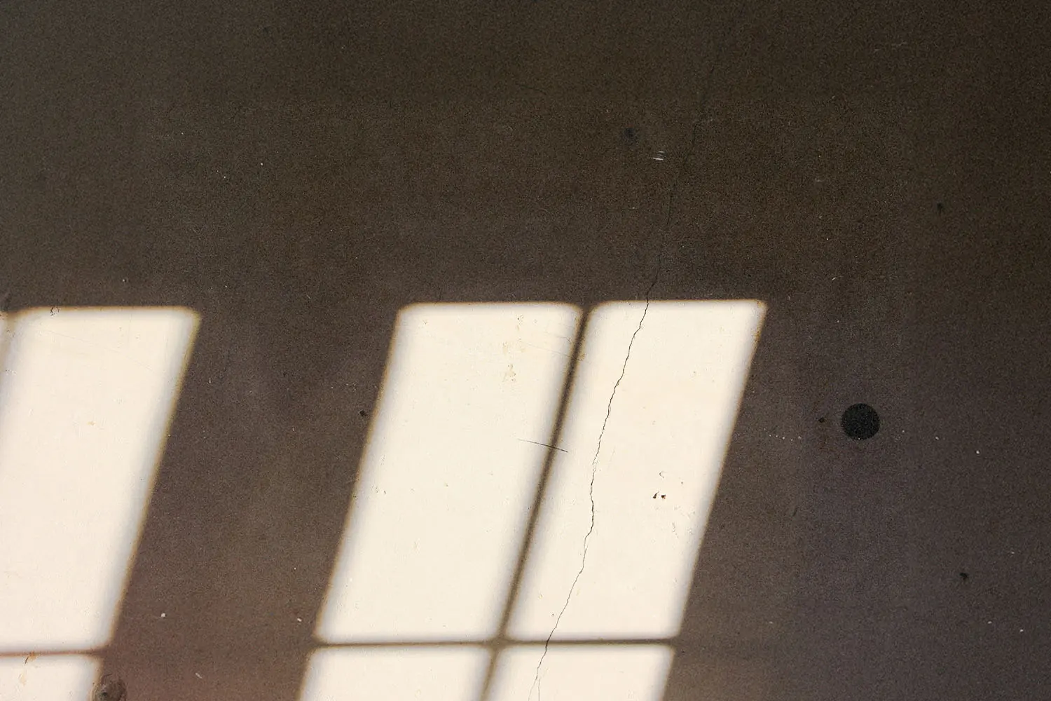 Rectangular window light casting three bright beams onto a textured wall with subtle cracks and shadows