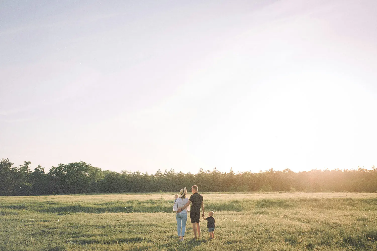 A family walking together through an open grassy field at sunset, holding hands and enjoying the warm light