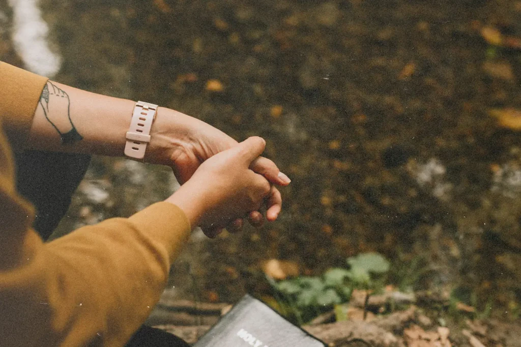 Hands clasped in prayer beside a closed Bible near a quiet stream in a natural setting