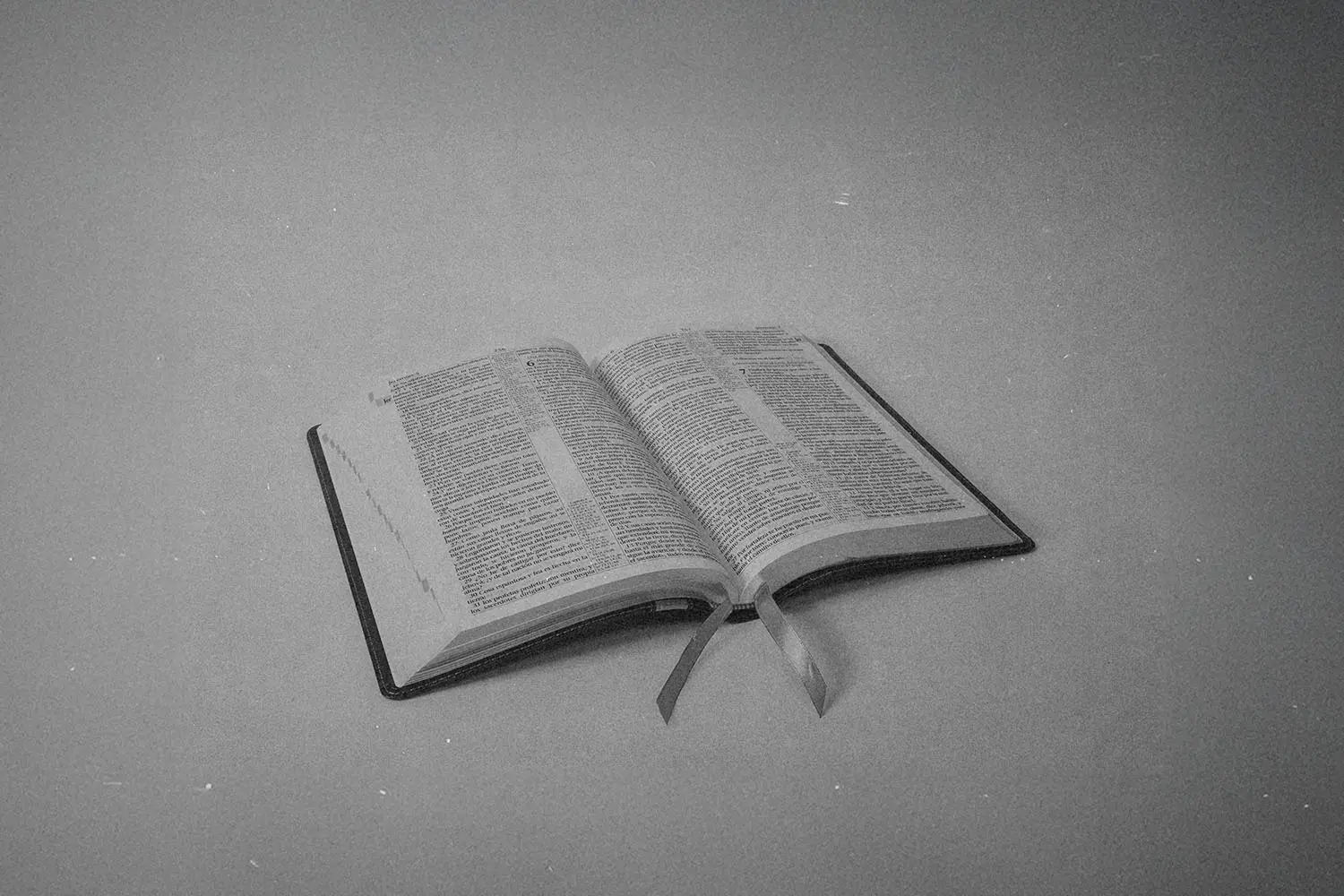 Black‑and‑white image of an open Bible resting on a flat surface with two ribbon bookmarks