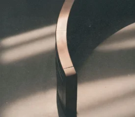 A curved wooden bench sits in soft, slanted sunlight, casting smooth shadows across the floor