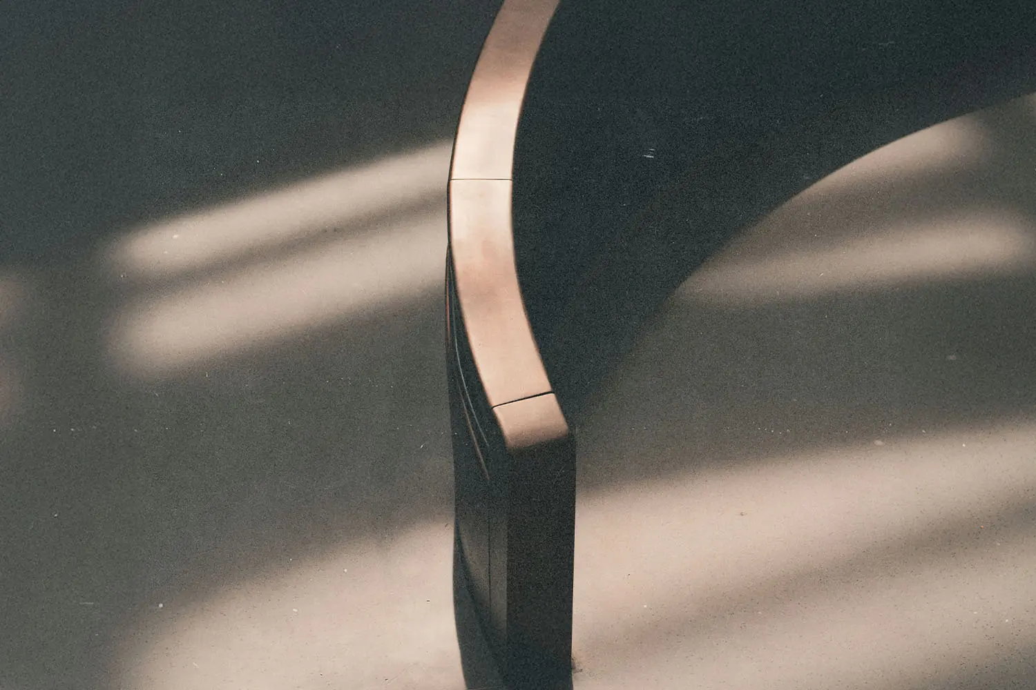 A curved wooden bench sits in soft, slanted sunlight, casting smooth shadows across the floor