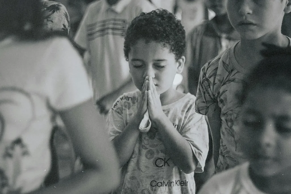 hild standing in a crowded room with hands held together in a prayer posture