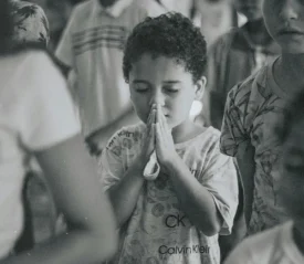 hild standing in a crowded room with hands held together in a prayer posture