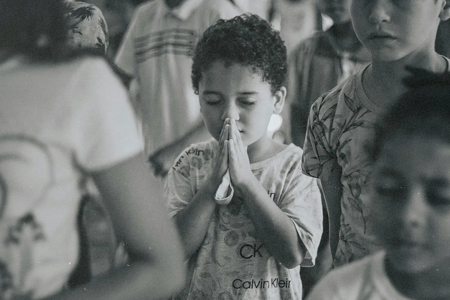 hild standing in a crowded room with hands held together in a prayer posture