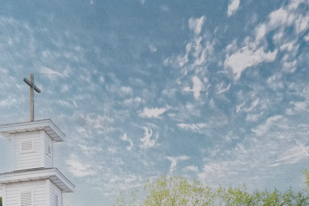 White church steeple with a cross on top set against a bright blue sky with scattered clouds
