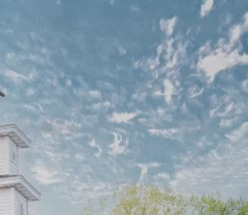 White church steeple with a cross on top set against a bright blue sky with scattered clouds
