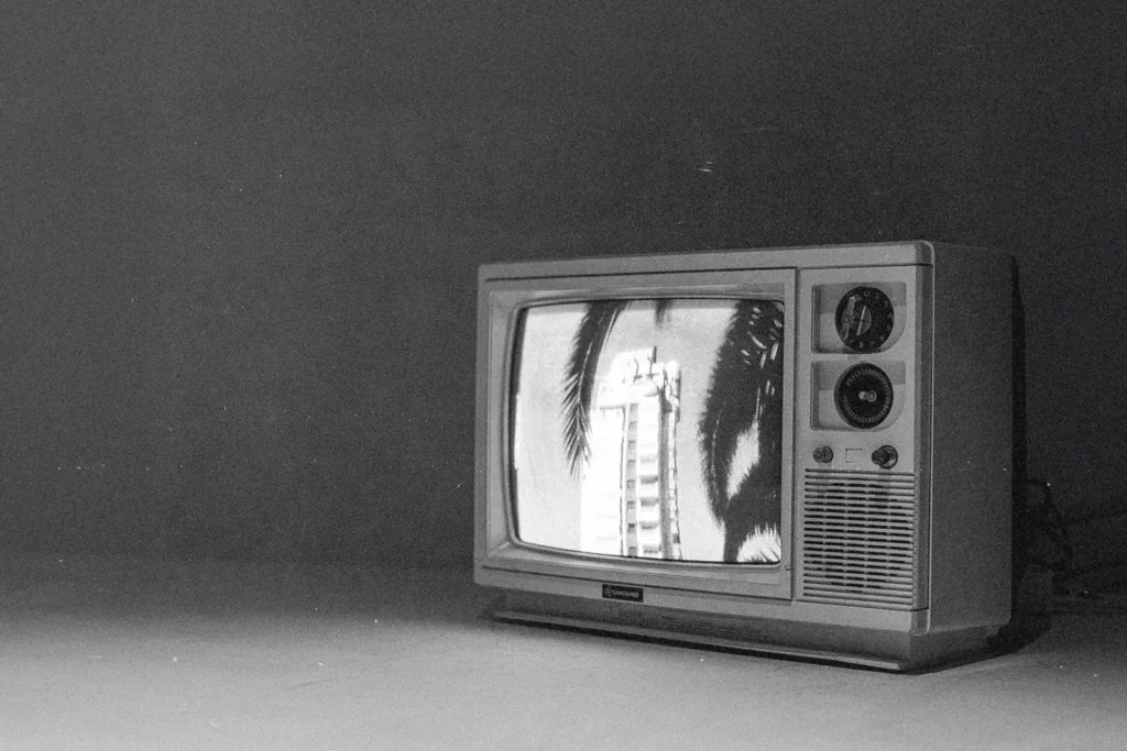 Vintage television sits in a dim room, displaying a black‑and‑white image of tall buildings framed by palm leaves