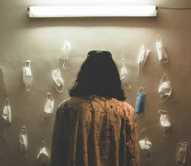 woman staring at a wall of tacked paper facemasks