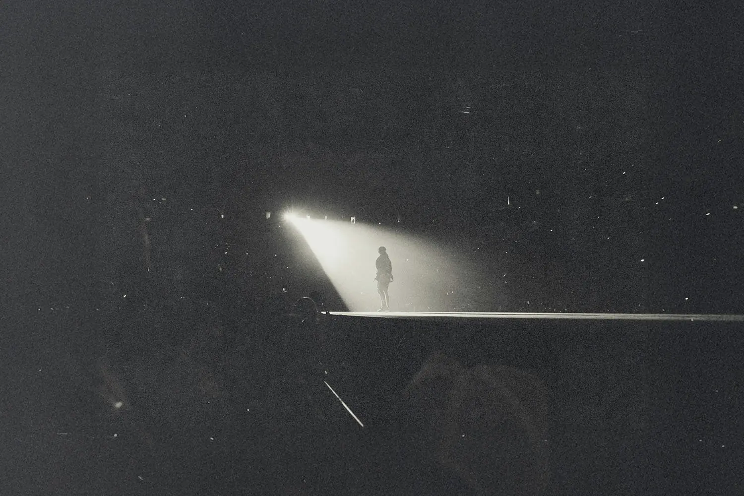 Silhouetted figure standing alone in a bright spotlight on a dark stage