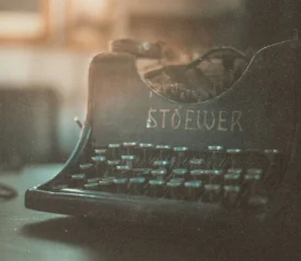 An old Stoewer typewriter sits on a dimly lit surface, with soft, warm light highlighting its worn keys and vintage metal frame