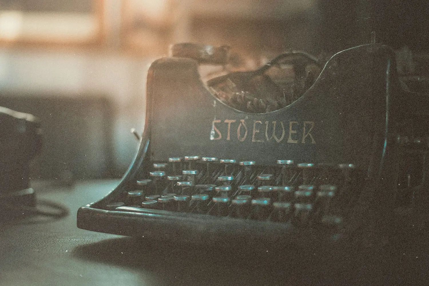 An old Stoewer typewriter sits on a dimly lit surface, with soft, warm light highlighting its worn keys and vintage metal frame