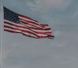 American flag waving on a tall flagpole against a partly cloudy blue sky