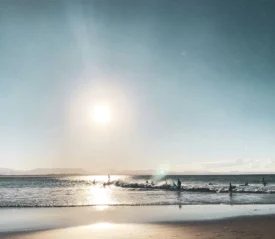 Bright sun above coastal waves with silhouettes of people in the water near the beach