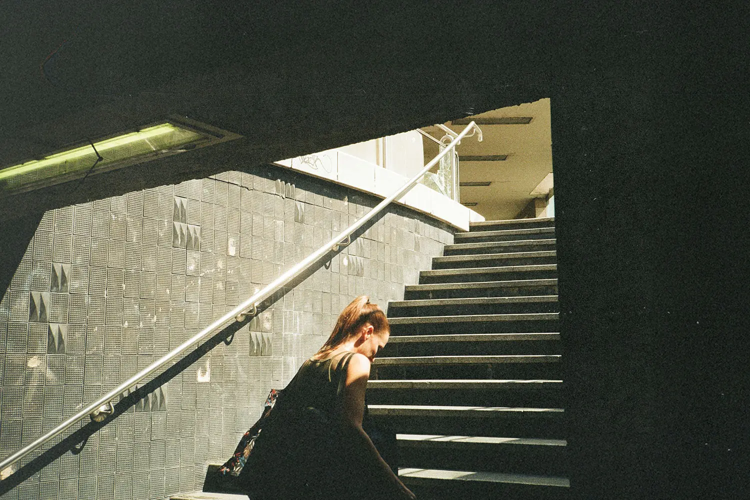 Person walking up a dimly lit stairway toward bright sunlight at the top of an urban underpass