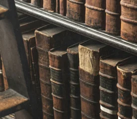 Close-up of old leather-bound books lined tightly on wooden shelves beside a worn wooden ladder