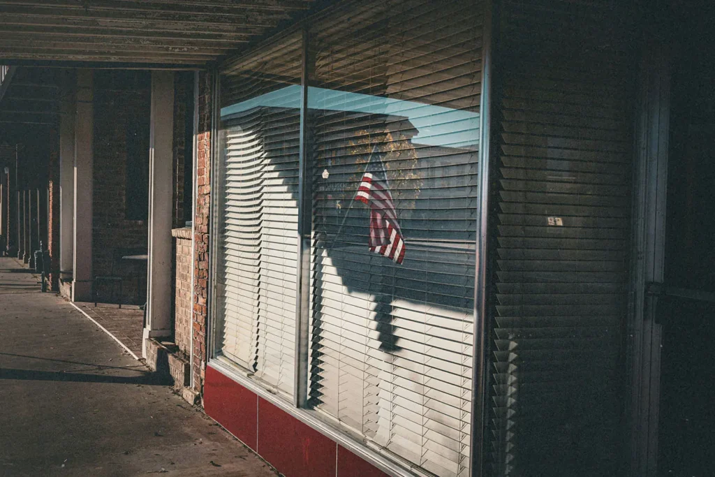 Window with open blinds and an American flag in the the glass reflection