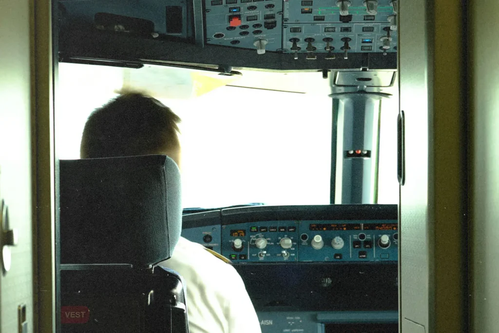 Back of the head of a pilot sitting at the head of the plane with controls