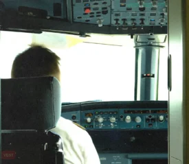 Back of the head of a pilot sitting at the head of the plane with controls