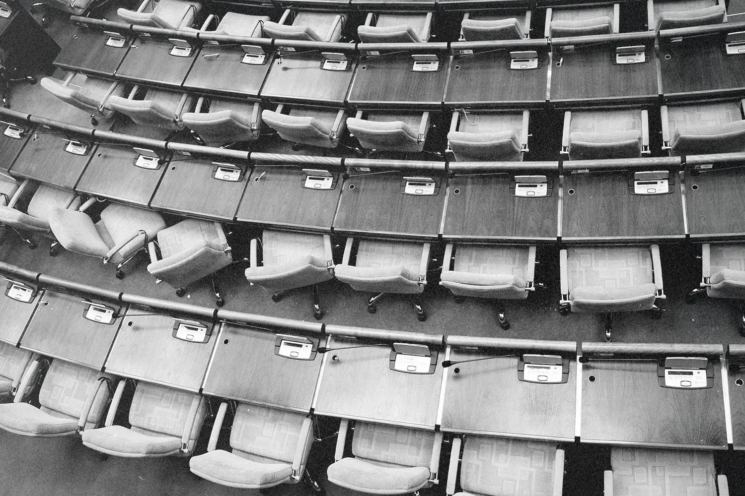 Rows of empty seats and wooden desks curve around an auditorium in a tiered arrangement