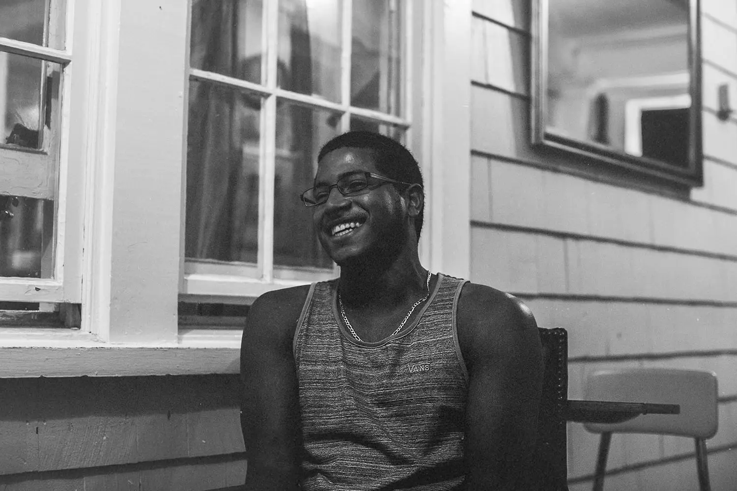 man laughing while sitting in a chair on a porch