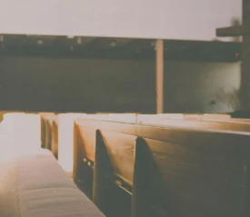 Sunlight streaming across empty wooden church pews with a large wooden cross at the front of the sanctuary