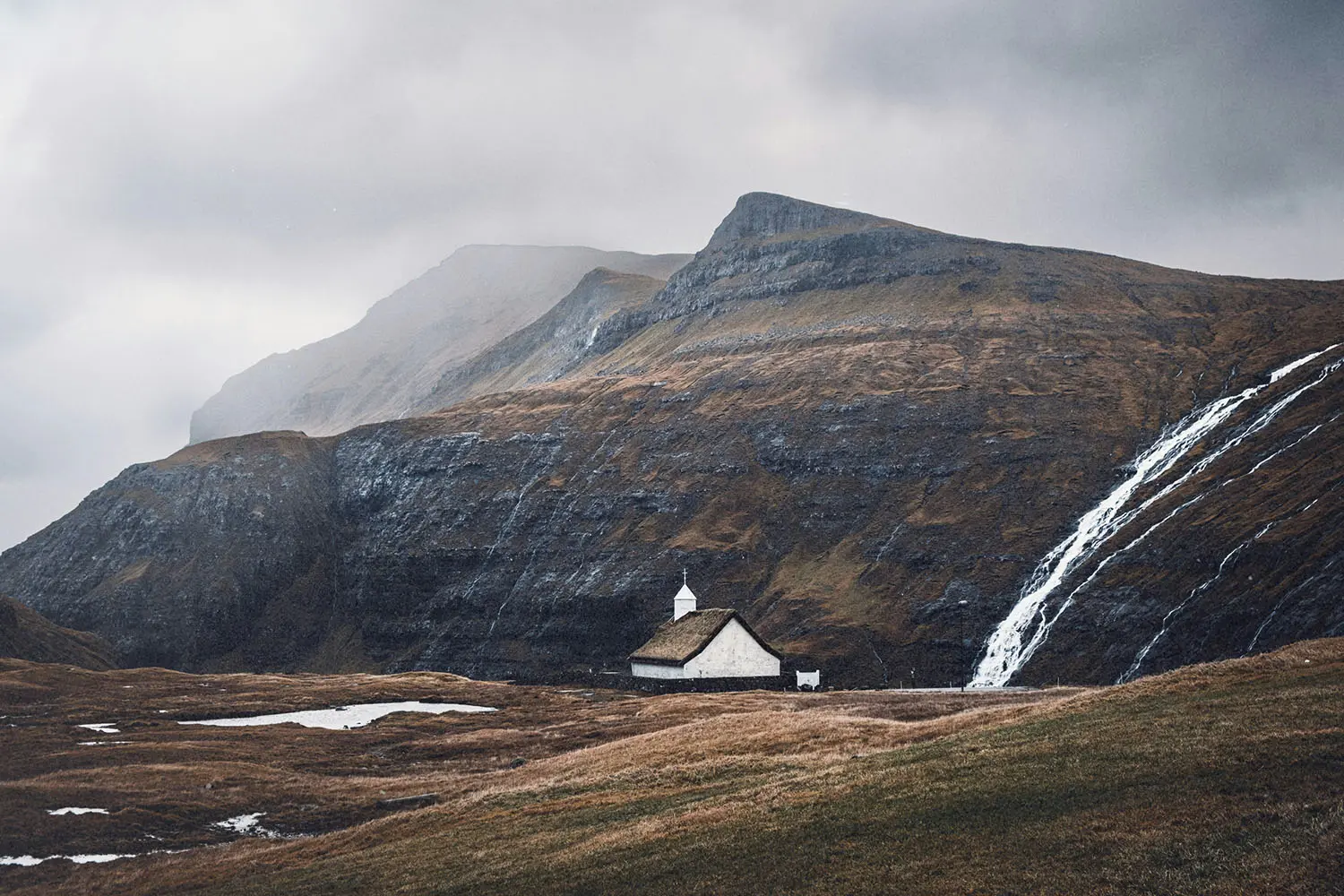 ll white church with a grass roof nestled in a vast mountain valley beside a cascading waterfall