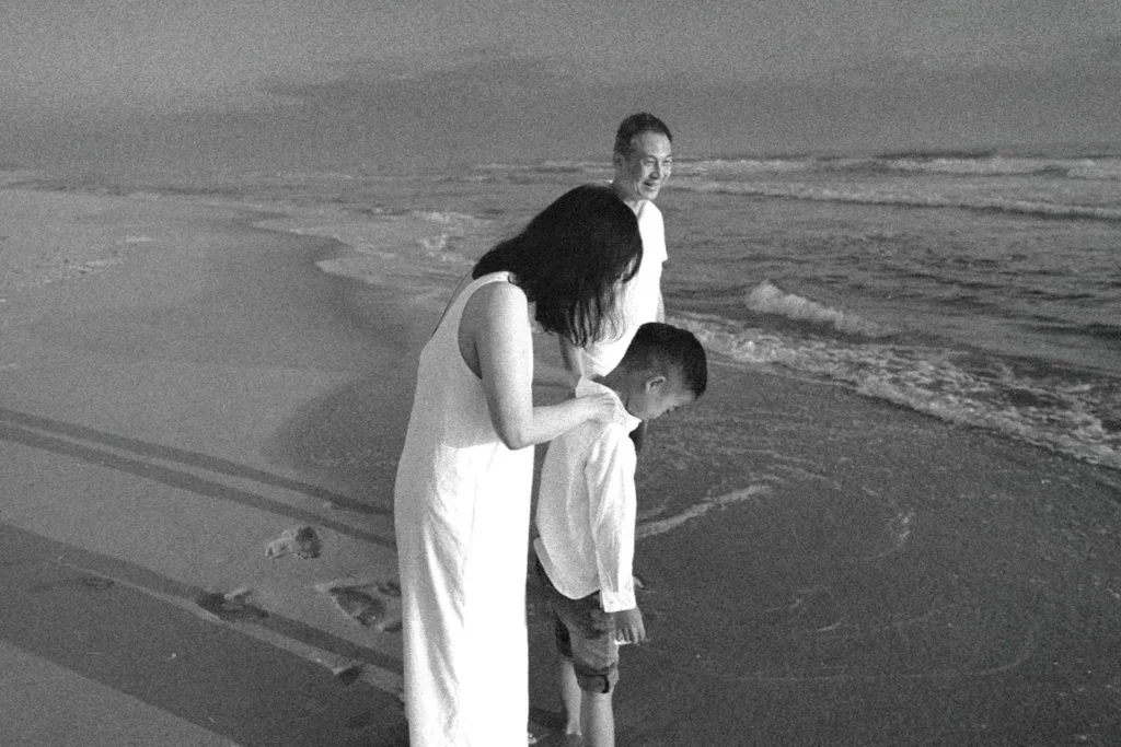 A family standing at the shoreline during sunset, with an adult gently comforting a child as waves reach their feet