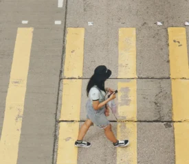 Person walking across a street with wide yellow crosswalk lines while holding a drink and looking at their phone
