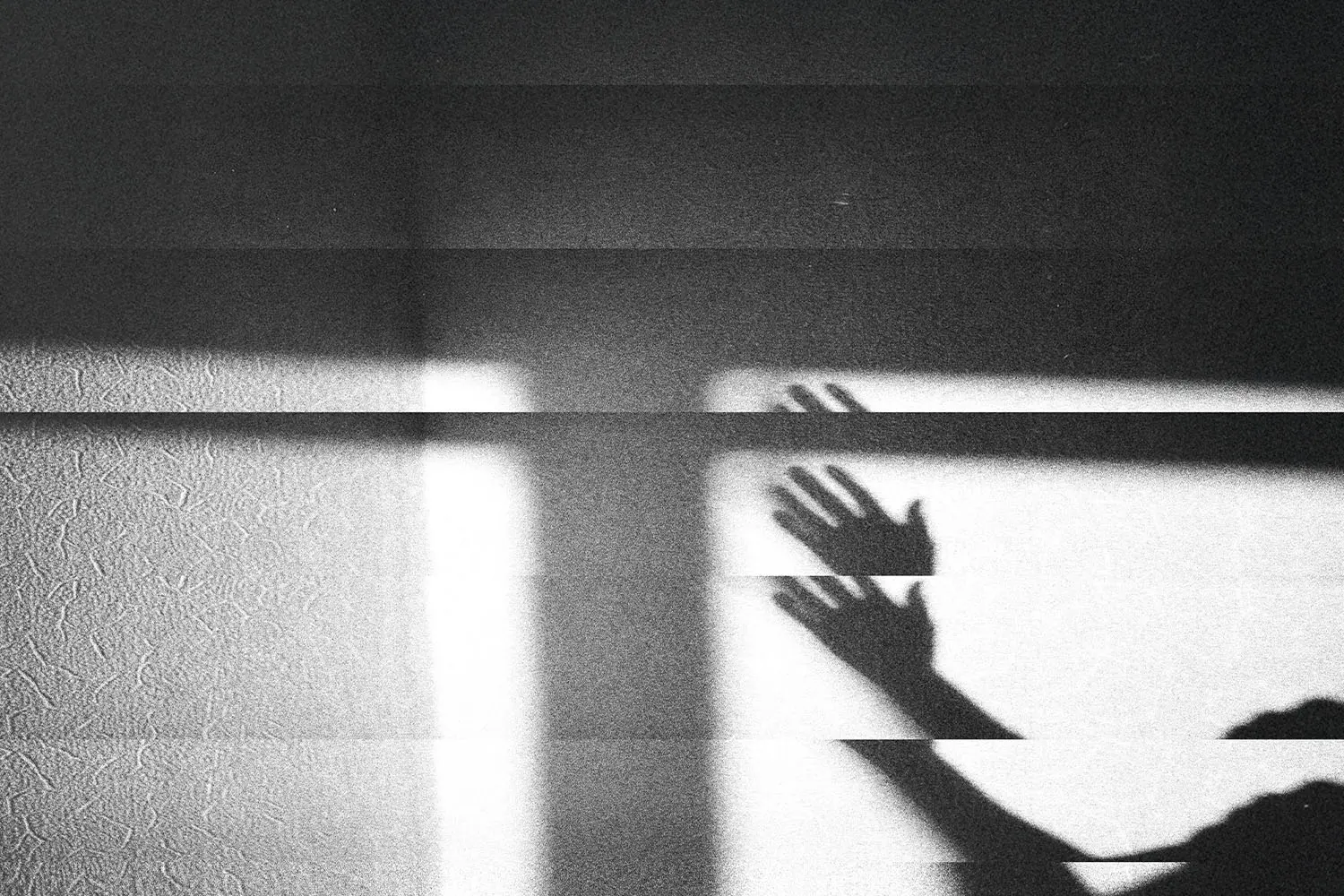 Shadow of raised hands cast across a textured wall in dramatic light and dark bands