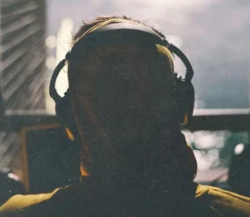 A person wearing large headphones is silhouetted against soft window light, with the background slightly out of focus