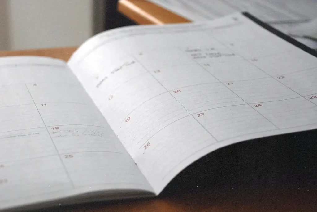 An open planner lies on a desk, showing a monthly calendar layout with faint handwritten notes