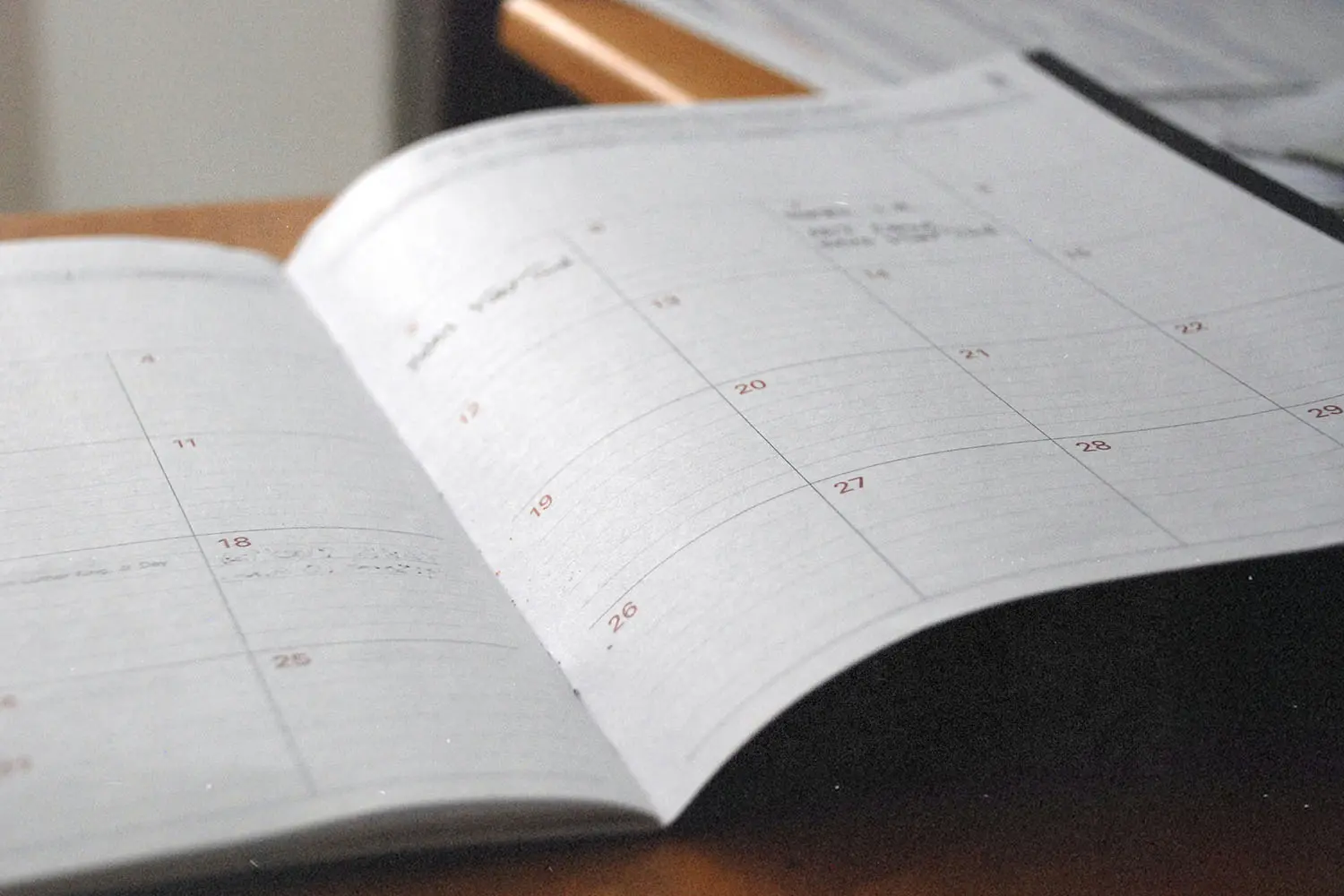 An open planner lies on a desk, showing a monthly calendar layout with faint handwritten notes