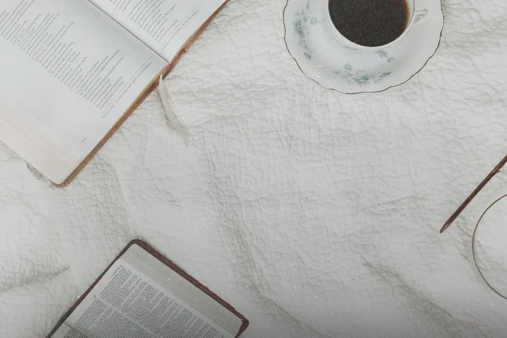 Two open books and a cup of coffee rest on a white quilted blanket