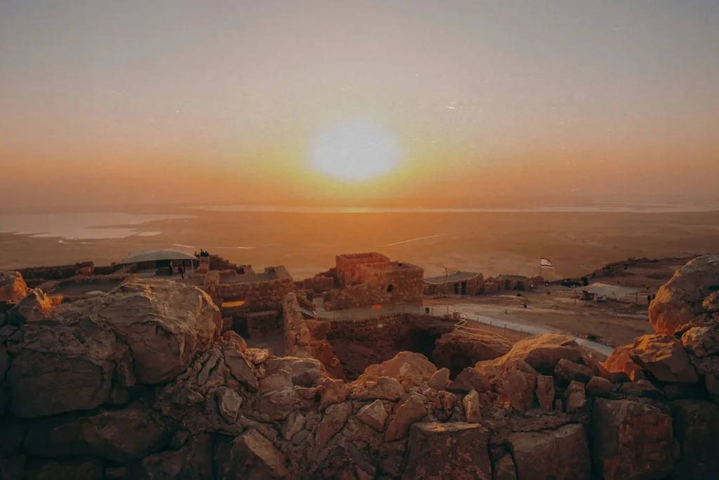 Sunset over ancient stone ruins atop a rocky desert plateau overlooking a distant body of water