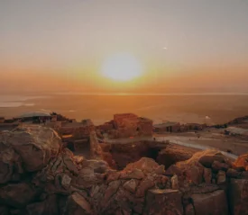 Sunset over ancient stone ruins atop a rocky desert plateau overlooking a distant body of water