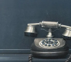 A vintage rotary telephone with a brass and wood finish sits against a dark matte background