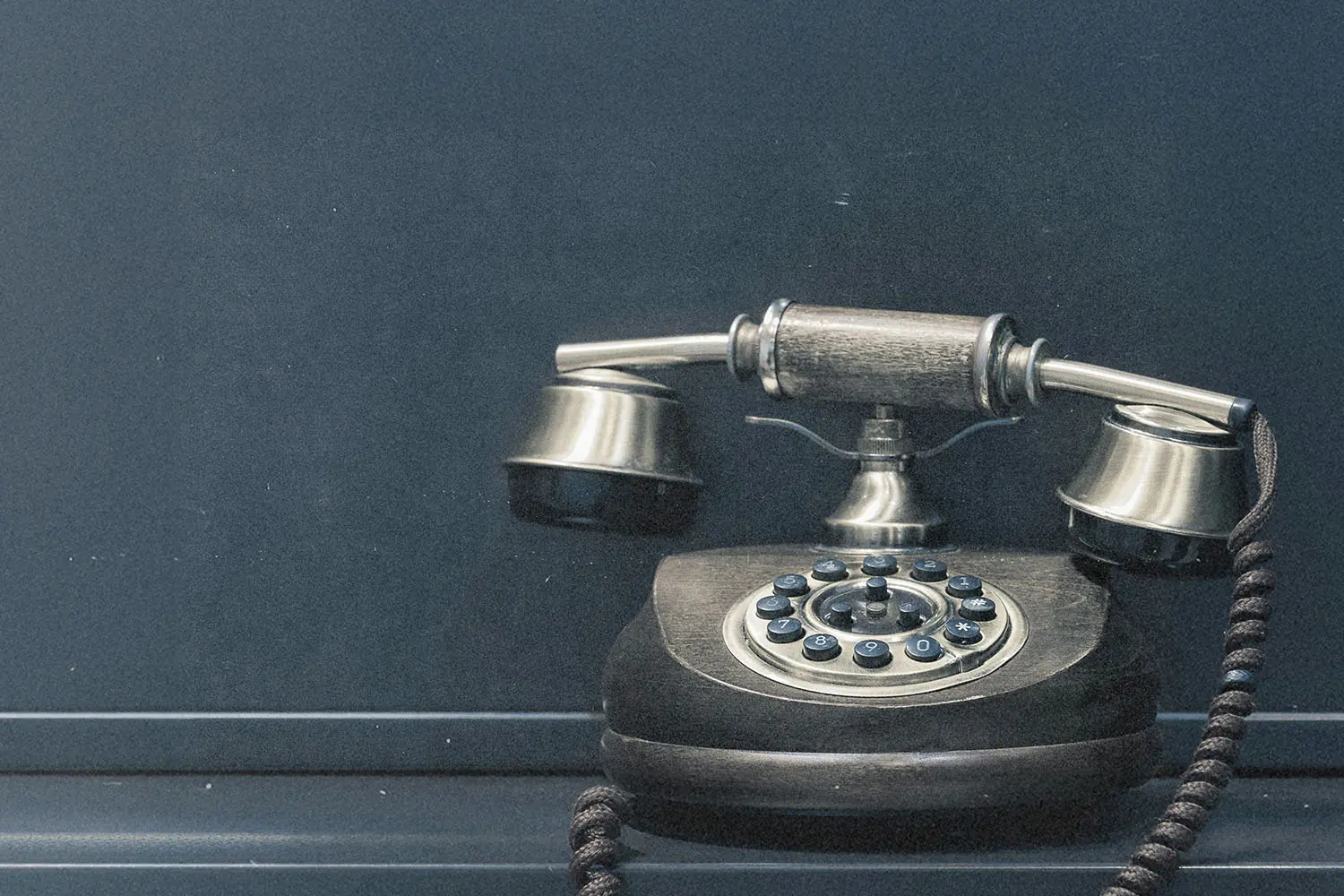 A vintage rotary telephone with a brass and wood finish sits against a dark matte background