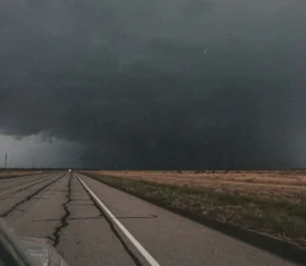 Road leading to gray skies with a tornado in the distance