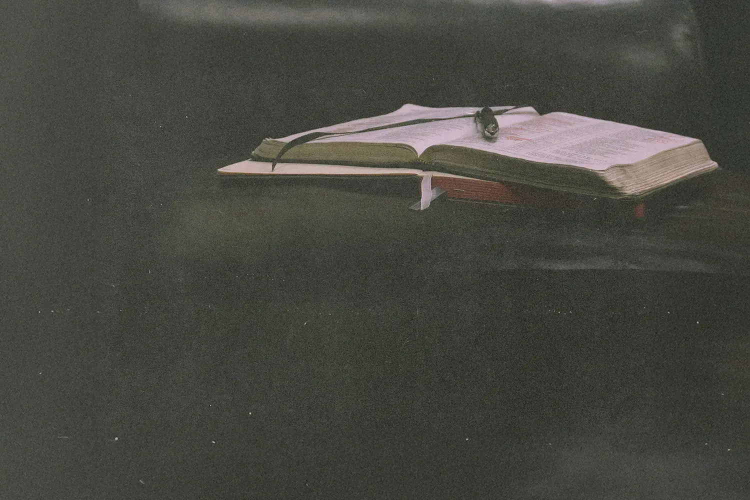 Open Bible resting on a dark leather surface with a ribbon marker and soft, moody lighting