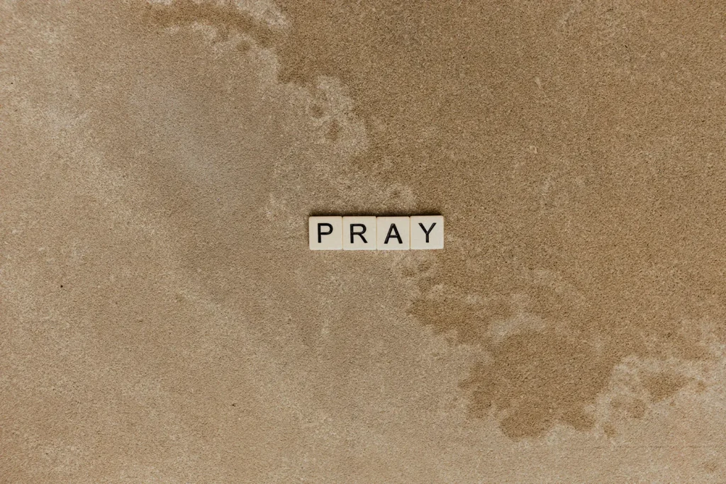 Scrabble letters spelling "PRAY" with an outline of a map in the background