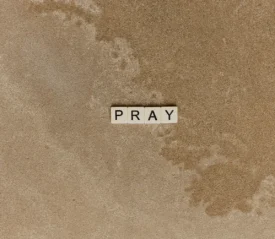 Scrabble letters spelling "PRAY" with an outline of a map in the background